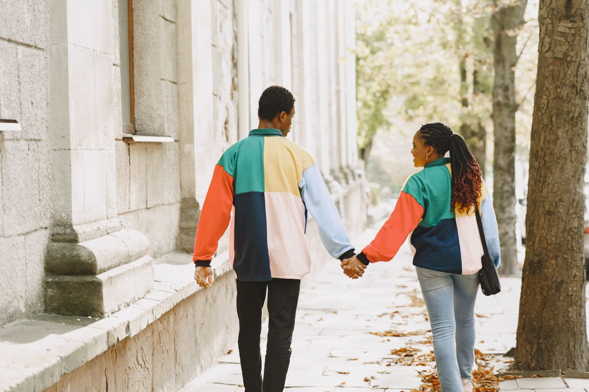 Un couple se tient la main dans une rue bordée d’arbres